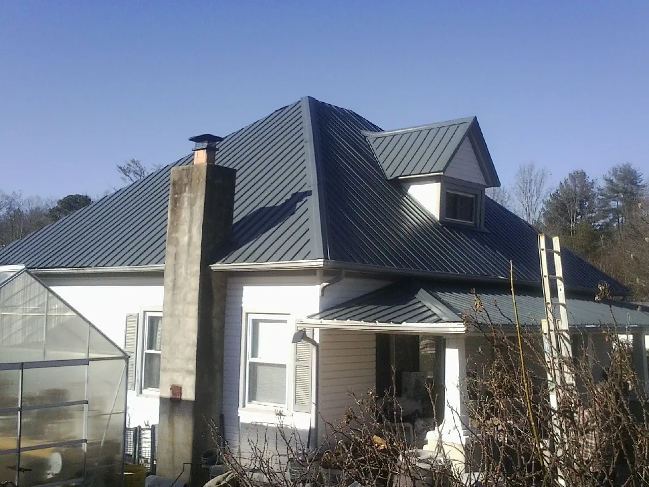 Dark blue standing seam metal roof on a white farmhouse with dormer — Slate & Tile Roof Repair by Roofing Brothers in Neeses