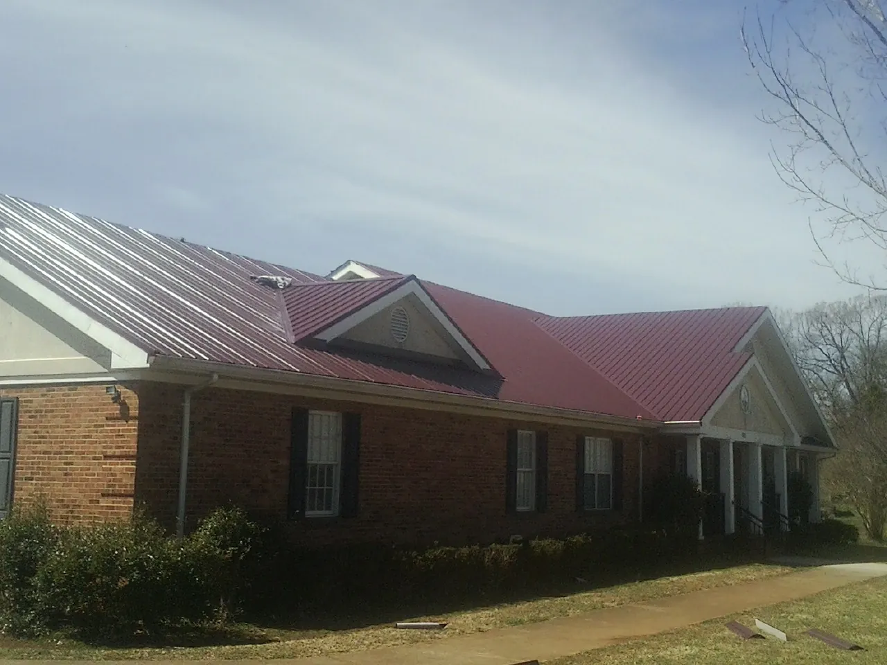 Red metal roof with gabled entries on a long brick building, from a Hail Damage Roof Repair job in Neeses