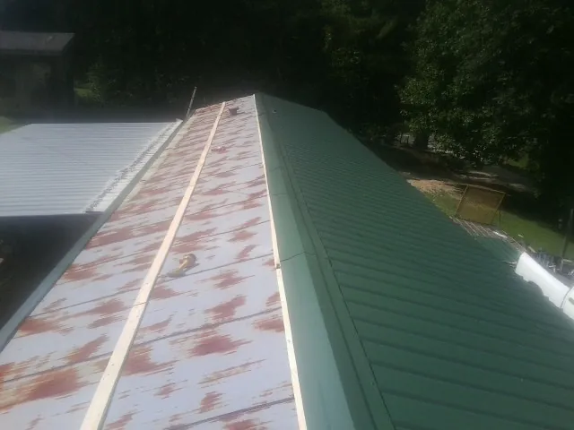 Old rusted panels beside newly installed green metal roofing — Wind Damage Roof Repair by Roofing Brothers in Neeses