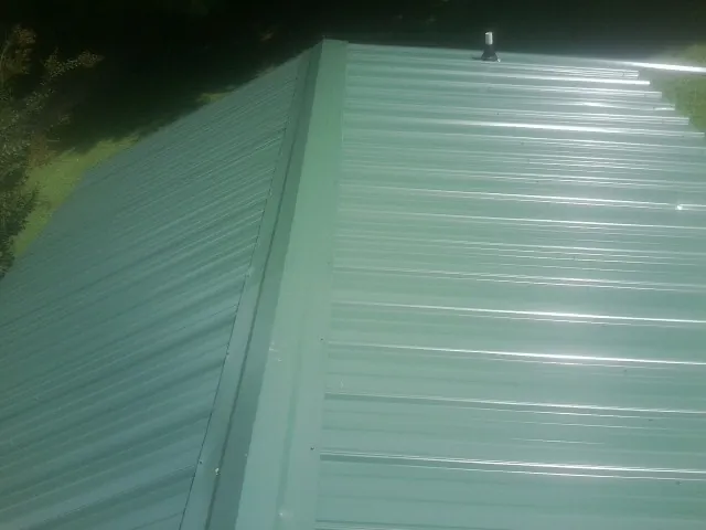 New green metal panels meeting at the ridge of a roof — Flat Roof Repair work by our crew in Neeses