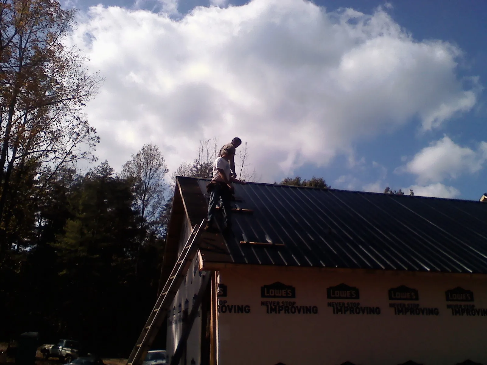 Roofer fastening dark metal panels high against a cloudy sky, from a Roof Inspection job in Neeses