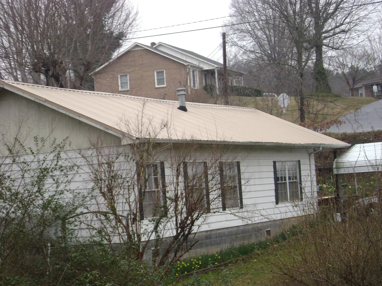 Tan metal roof on a white sided house set into a hillside — Commercial Roofing by Roofing Brothers in Neeses