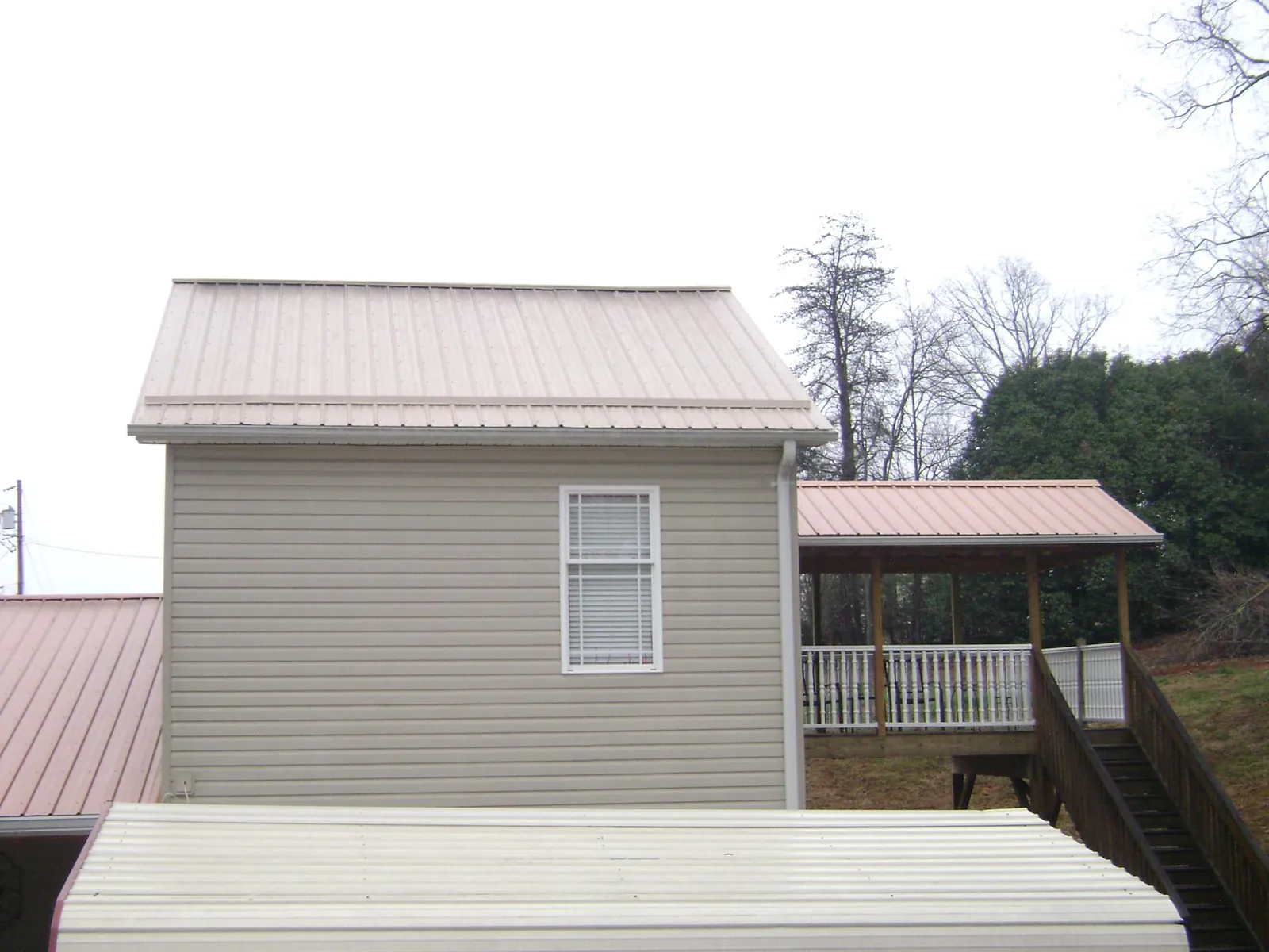 Tan metal roofs on a two story addition and attached porch, from a Roof Replacement job in Neeses